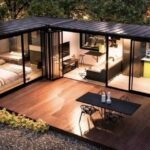 The Ridge container home at night, an L-shaped layout with lit interiors and a wraparound deck